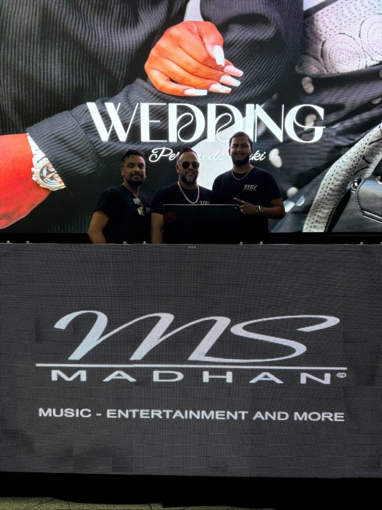 Drei Personen stehen vor einer großen Anzeige mit dem Text "Wedding".